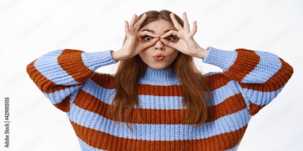 Funny cute girl look through hand binoculars, pucker lips, saying wow,  making glasses gesture around eyes and staring at camera, standing in  sweater against white background Photos | Adobe Stock